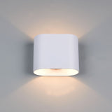 A modern cylindrical wall sconce light fixture in matte white, mounted on a light gray wall and casting a warm glow upwards and downwards.