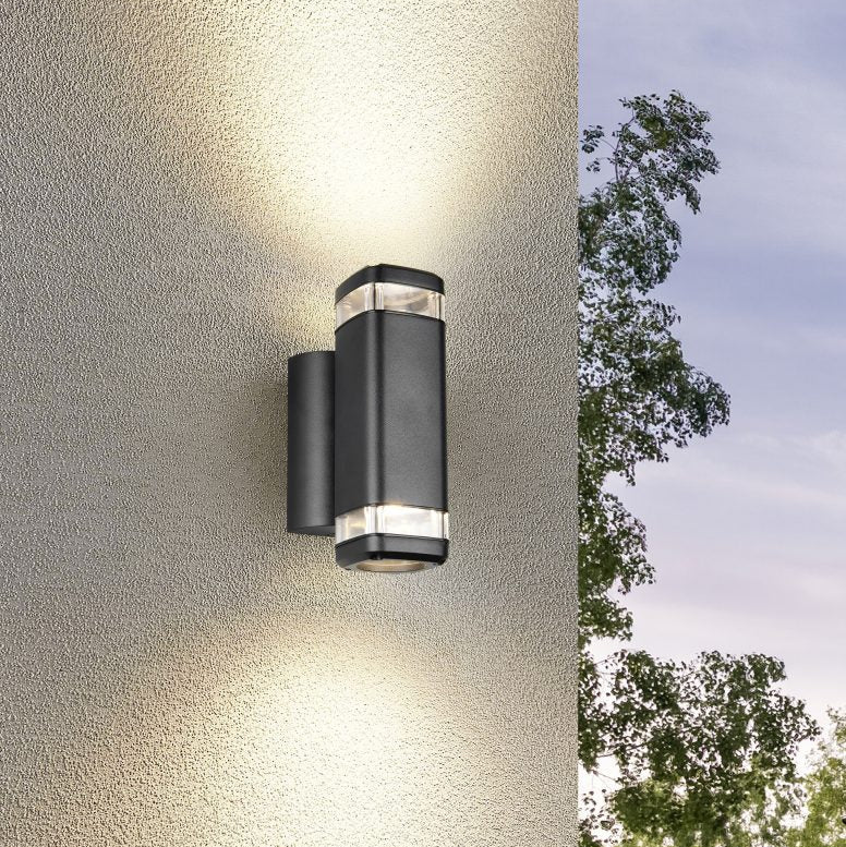 Black outdoor wall light fixture on a textured wall with trees in the background