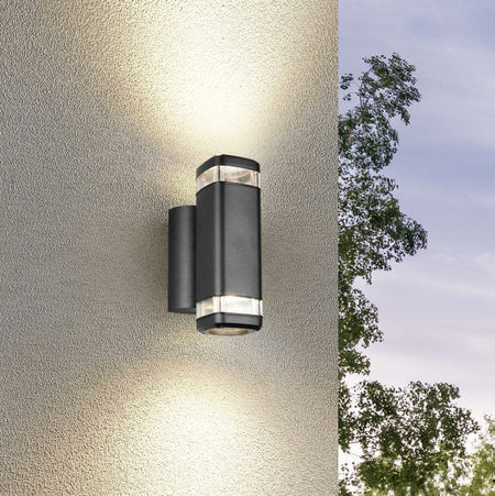 Black outdoor wall light fixture on a textured wall with trees in the background
