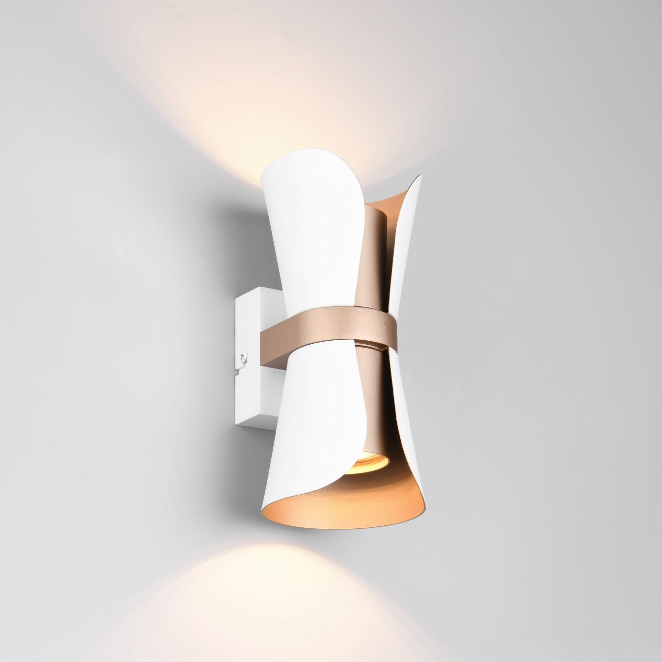 A modern wall-mounted sconce with a white sculptural curved shade, a warm metallic band around the middle, and a glowing light emitted downward and upward against a light gray wall.