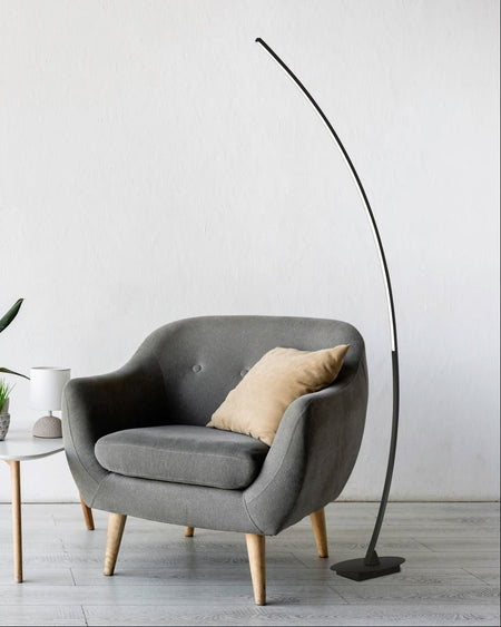 Modern living room with a gray armchair, floor lamp, and abstract paintings on a white wall.